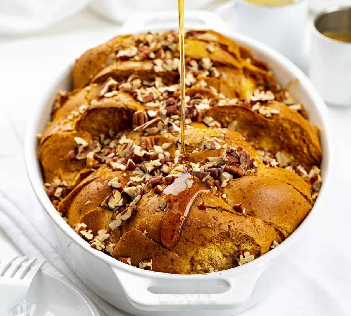 Adding Syrup to Pumpkin French Toast Casserole in White Pan on White Counter.