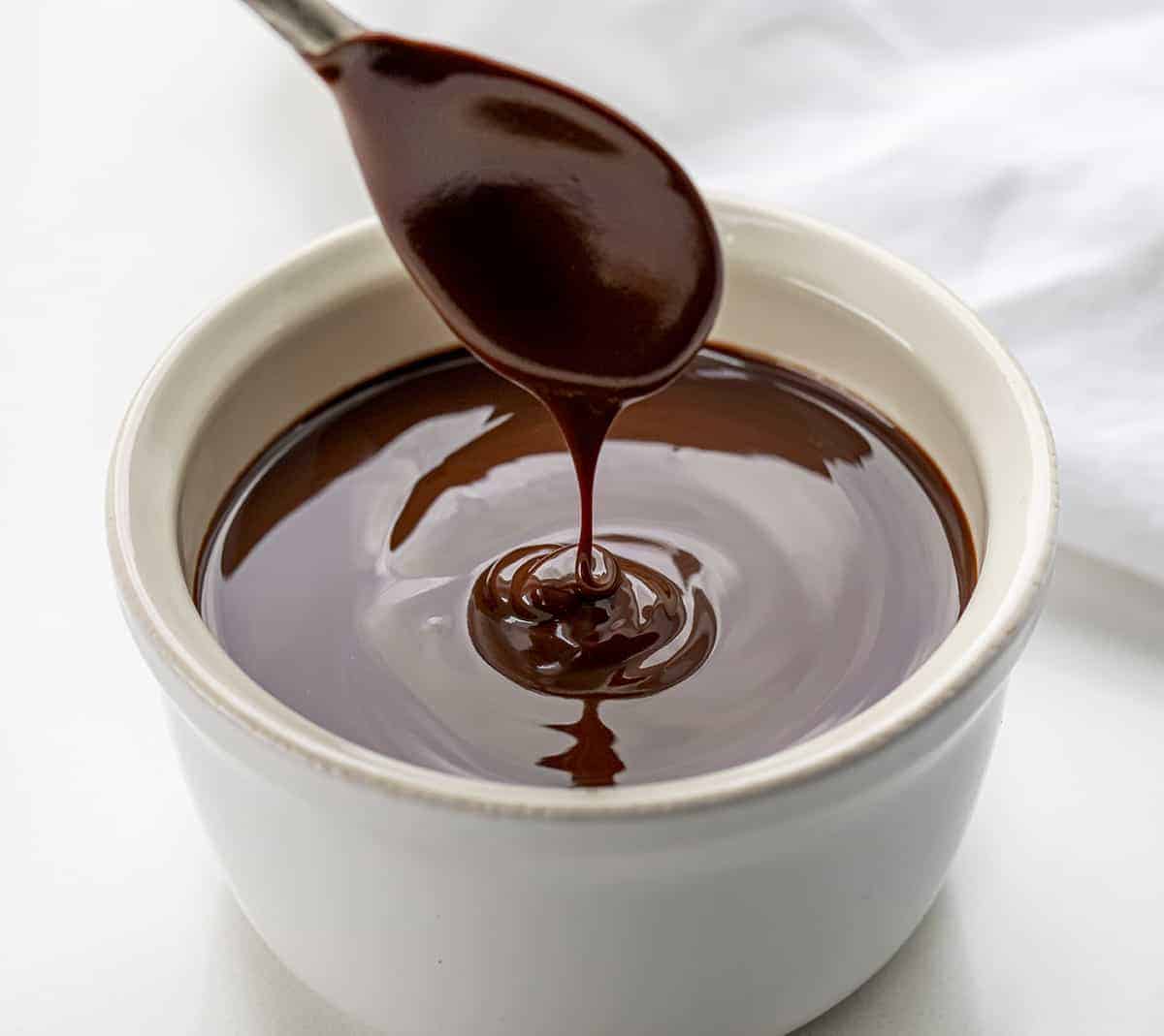 Chocolate Ganache made with Butter is semi-sweet chocolate melted with butter to create a rich and shiny chocolatey topping, glaze, icing, or filling. 2 ingredient ganache, two ingredient ganache, butter chocolate ganache, butter ganache, chocolate ganache, easy chocolate ganache, how to make ganache, the best butter ganache recipes, desserts, baking, chocolate, easter, new years eve, christmas ganache, i am baker, iambaker Spoon with Butter Chocolate Ganache Drizzling the Ganache