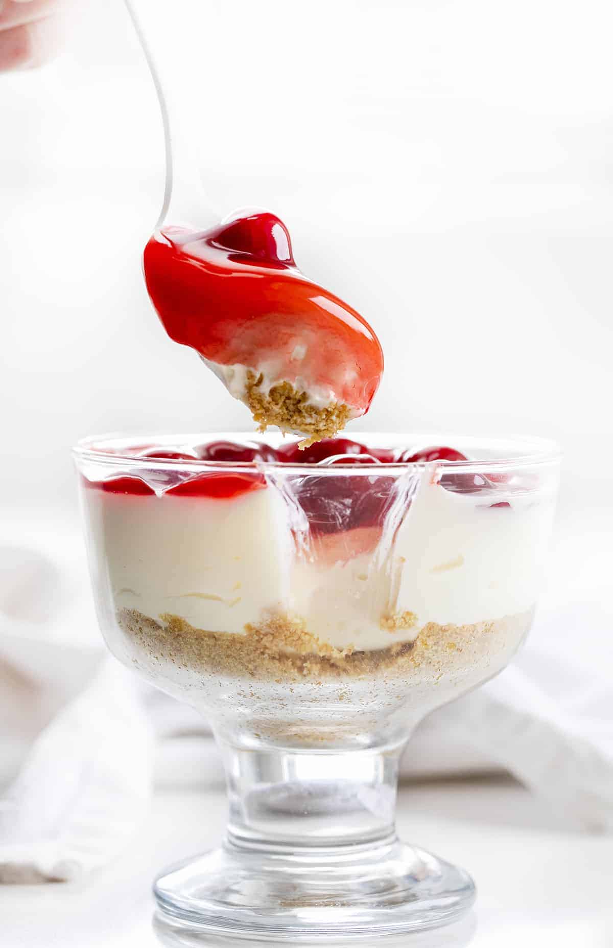No-Bake Cherry Cheesecake Parfaits are a cheesecake dessert with a graham cracker crust and cherry pie topping, all served in a cup! Dessert, No Bake Dessert, Cherry Cheesecake, Cheesecake Parfait, Cherry Cheesecake Parfait, Cheesecake in a Cup, Creamy Cheesecake, BBQ Dessert, Cookout Dessert, i am baker, iambaker Spoon Taking a Bite out of No-Bake Cherry Cheesecake Parfait.