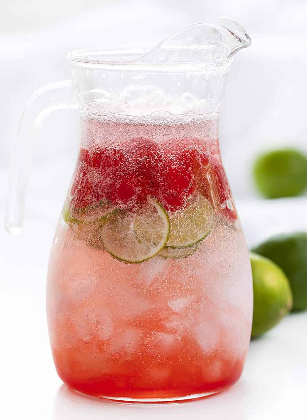 Cherry Limeade is a cold, refreshing non-alcoholic drink that is made with fresh lime juice, Sprite, and maraschino cherries, all poured over crushed ice! Cherry Limeade, Beverages, Non-Alcoholic Cocktails, Drinks, Drink Recipes, BBQ, How to Make Cherry Limeade, Sonic Copycat Limeade, Cherry Drinks, i am baker, iambaker, drink recipes Pitcher of Homemade Cherry Limeade Drink with Fresh Limes in Back