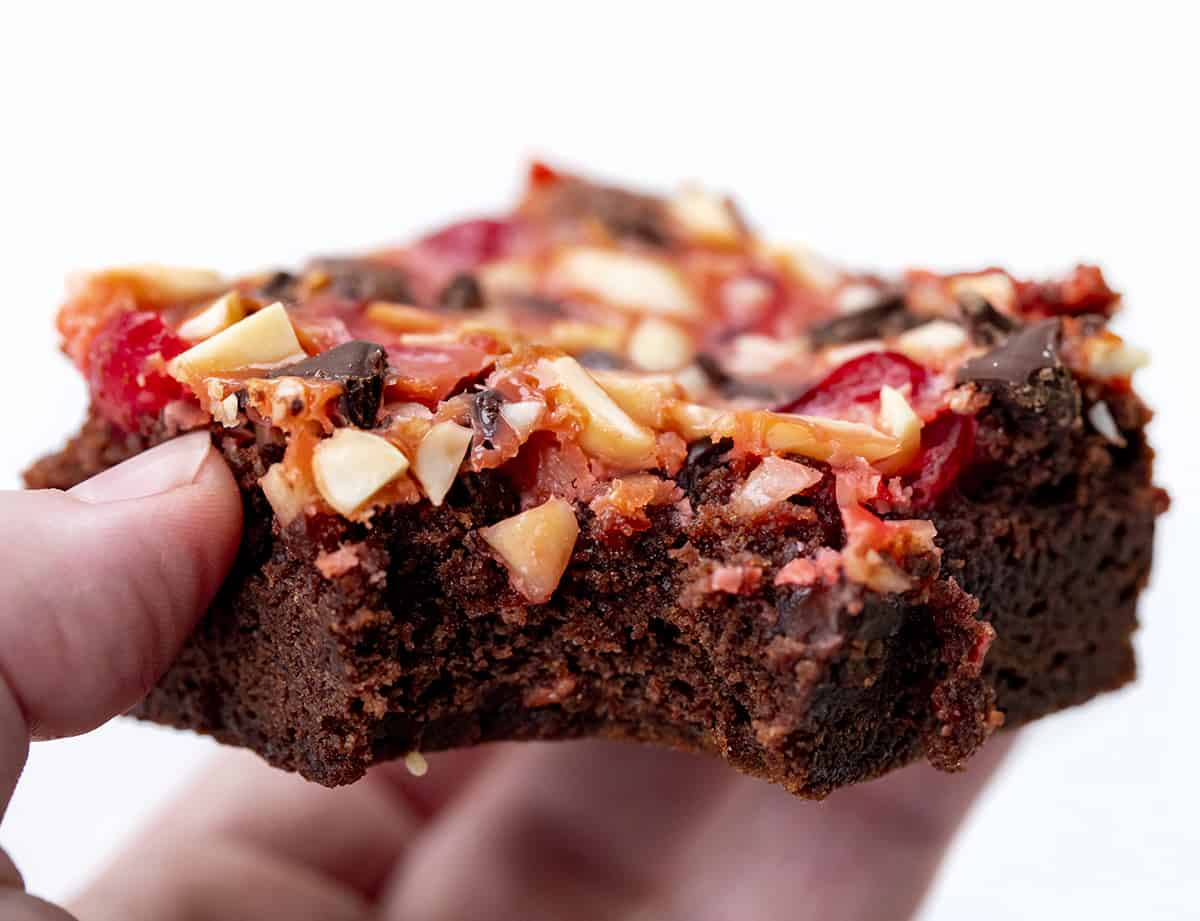 Hand holding bit into Cherry Chocolate Magic Brownies.