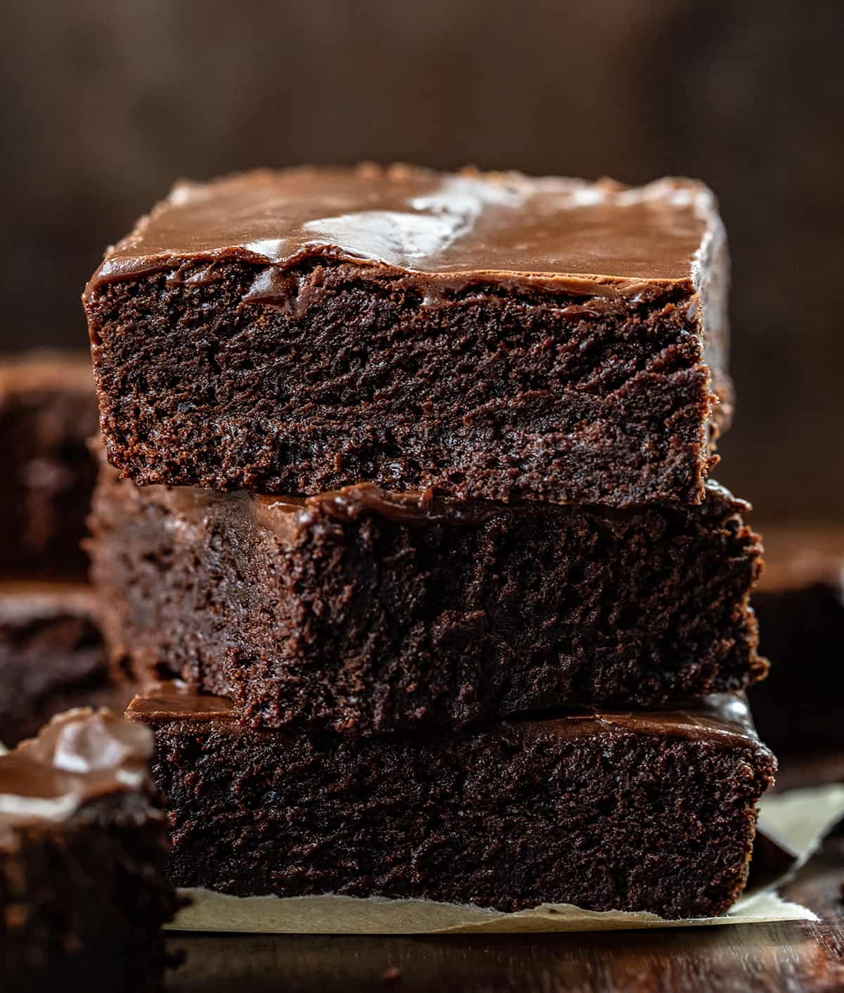This is the ONLY true Double Fudge Brownie!! Once you take a bite you'll know exactly why I can say that. This Double Fudge Brownie has a moist, luscious texture with an intense chocolate flavor in every deliciously chewy and fudgy bite! Although these brownies can stand on their own, I added a brownie frosting to make this treat even more decadent. Three Double Fudge Brownies Stacked on Top of Each Other on a Dark Cutting Board.