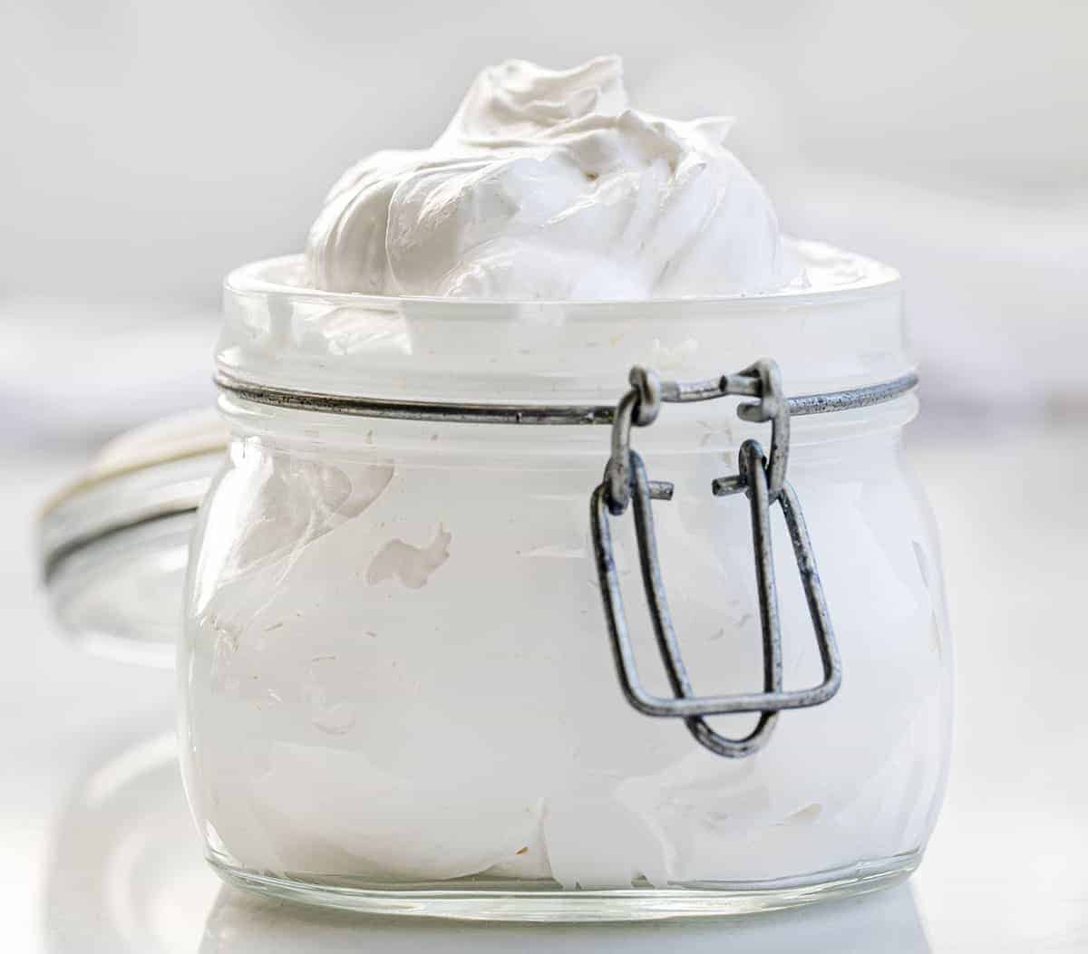 Marshmallow Fluff, or Marshmallow Creme, is not even made with marshmallows, but it has a similar flavor. Sweet gooey deliciousness! Marshmallow Fluff, How to Make Fluff, Homemade Fluff, What is in marshmallow fluff, Is there marshmallow in marshmallow fluff, fudge with homemade fluff, dessert, no bake dessert, cake topping, recipes, i am baker, iambaker Jar of Homemade Marshmallow Fluff on White Counter
