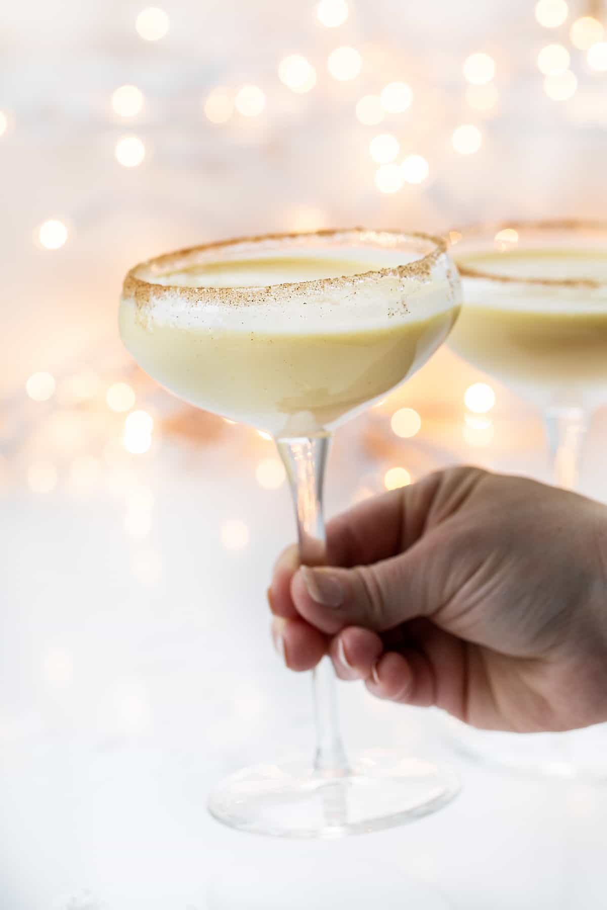Rumchata Eggnog is an alcoholic beverage made with eggnog and RumChata® served in a glass with a cinnamon-sugar rim. It's the perfect cocktail to serve at your Christmas and New Year's Eve parties! Hand Picking up a Glass of RumChata Eggnog.