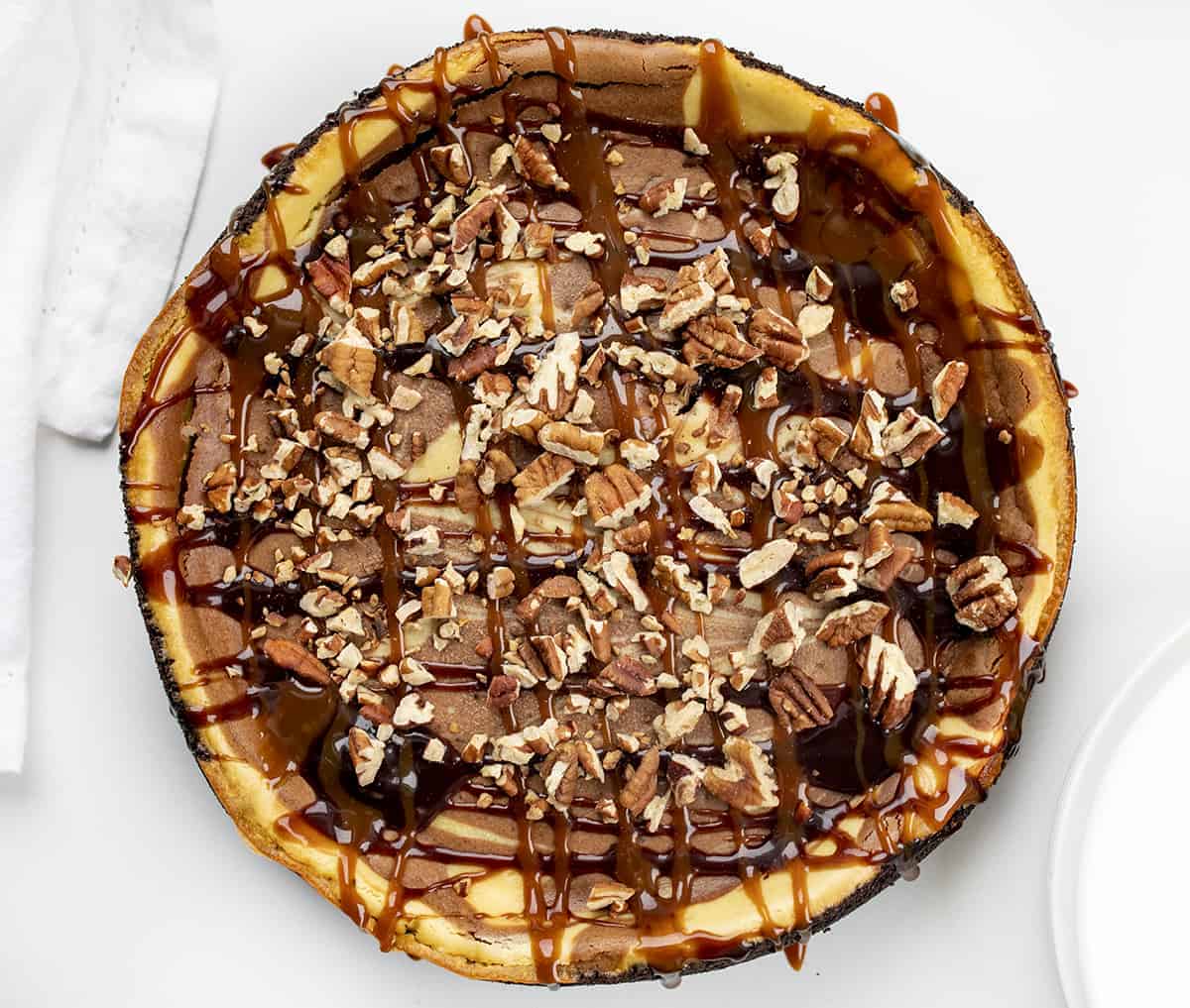 Turtle Cheesecake is a dessert with an Oreo cookie and toasted pecans crust, filled with a chocolate-swirled cheesecake filling and topped with caramel, hot fudge, and more pecans. Cheesecake Recipe, Turtle Cheesecake, Chocolate Caramel Cheesecake, Easy Cheesecake, Ultimate Cheesecake, Holiday Desserts, Dessert, recipes, baking, i am baker, iambaker Overhead of a Whole Turtle Cheesecake