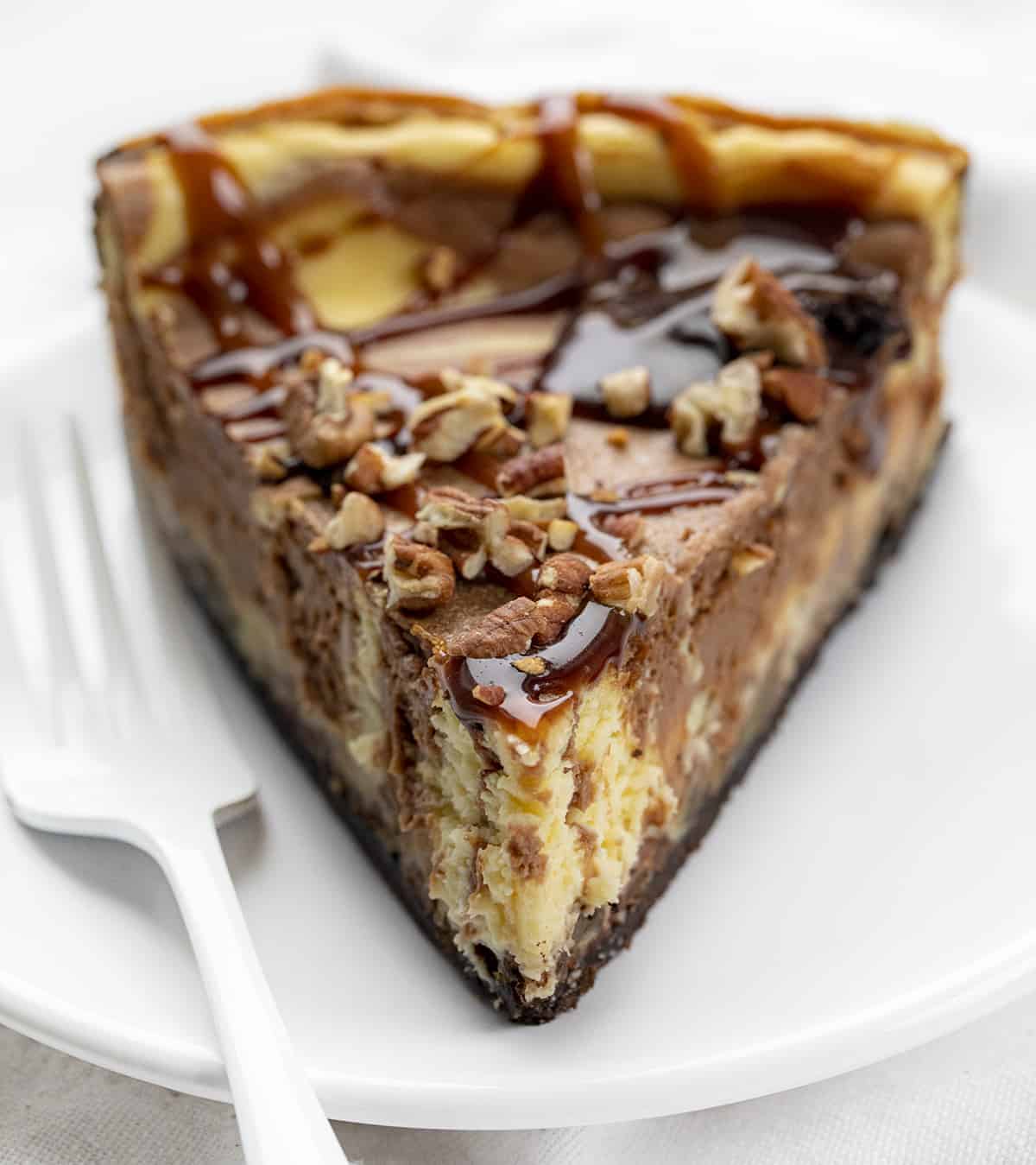 Turtle Cheesecake is a dessert with an Oreo cookie and toasted pecans crust, filled with a chocolate-swirled cheesecake filling and topped with caramel, hot fudge, and more pecans. Cheesecake Recipe, Turtle Cheesecake, Chocolate Caramel Cheesecake, Easy Cheesecake, Ultimate Cheesecake, Holiday Desserts, Dessert, recipes, baking, i am baker, iambaker Slice of Turtle Cheesecake