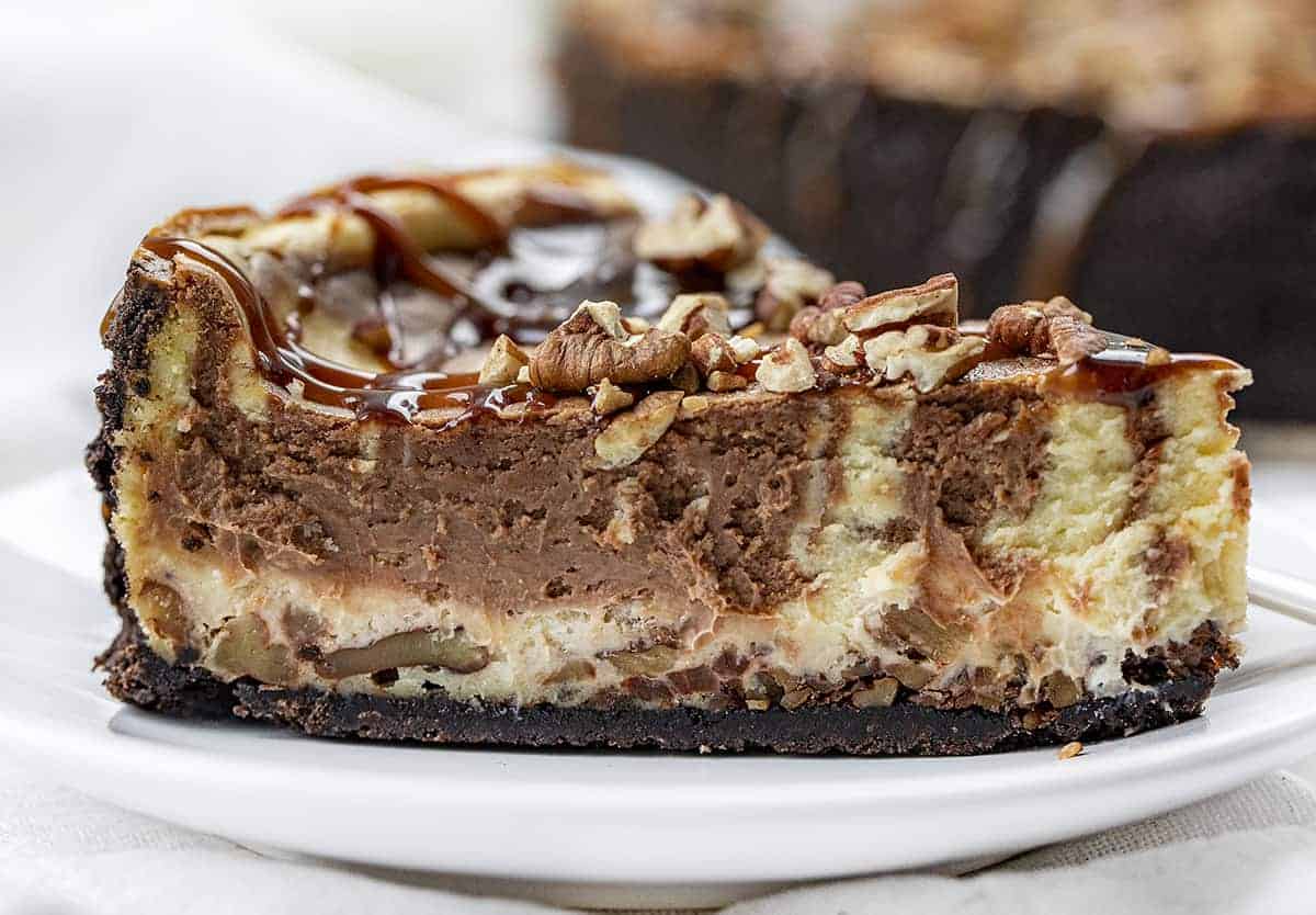 Turtle Cheesecake is a dessert with an Oreo cookie and toasted pecans crust, filled with a chocolate-swirled cheesecake filling and topped with caramel, hot fudge, and more pecans. Cheesecake Recipe, Turtle Cheesecake, Chocolate Caramel Cheesecake, Easy Cheesecake, Ultimate Cheesecake, Holiday Desserts, Dessert, recipes, baking, i am baker, iambaker Slice of Turtle Cheesecake Showing Inside